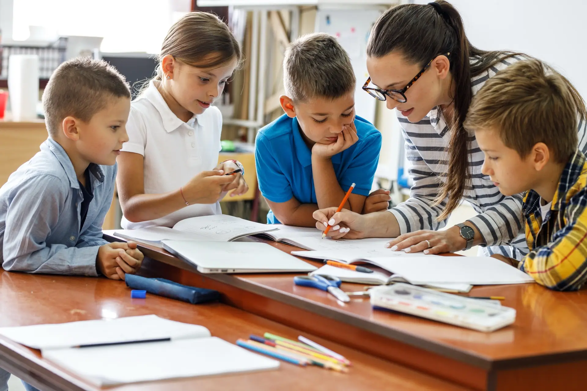 Junge Lehrerin schreibt in ein Heft umringt von Schülern.